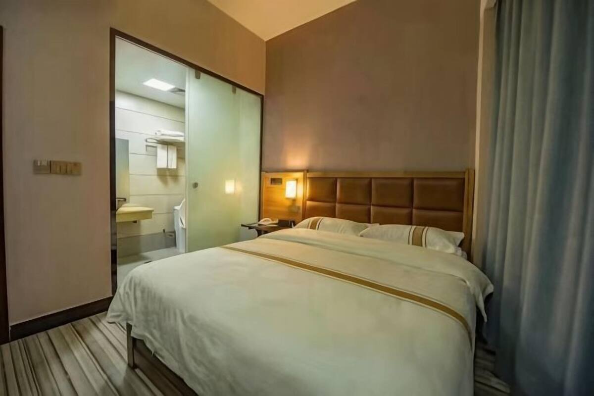A hotel room with a bed, a bedside table, a mirror, and a bathroom visible through an open door.