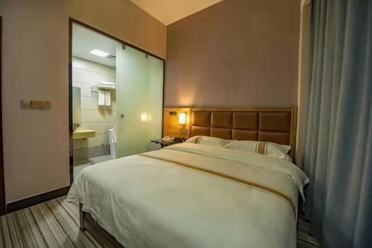 A hotel room with a bed, a bedside table, a mirror, and a bathroom visible through an open door.