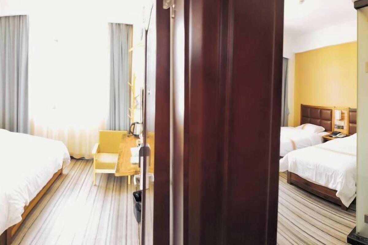 A hotel room with two beds, a wooden floor, a desk with a chair, and a small table with a lamp.