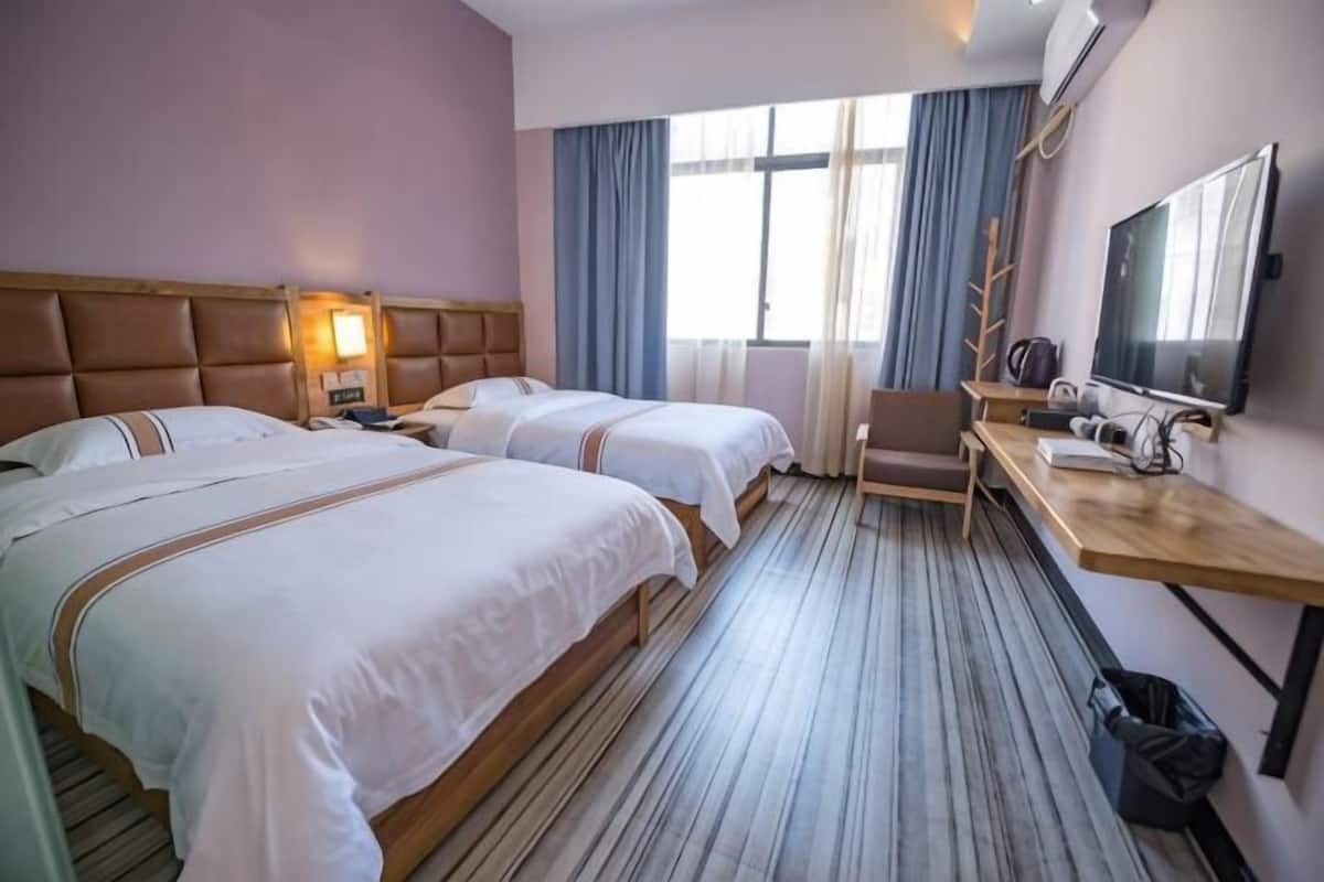 A hotel room with two beds, a desk, a chair, a TV, and a window with curtains.