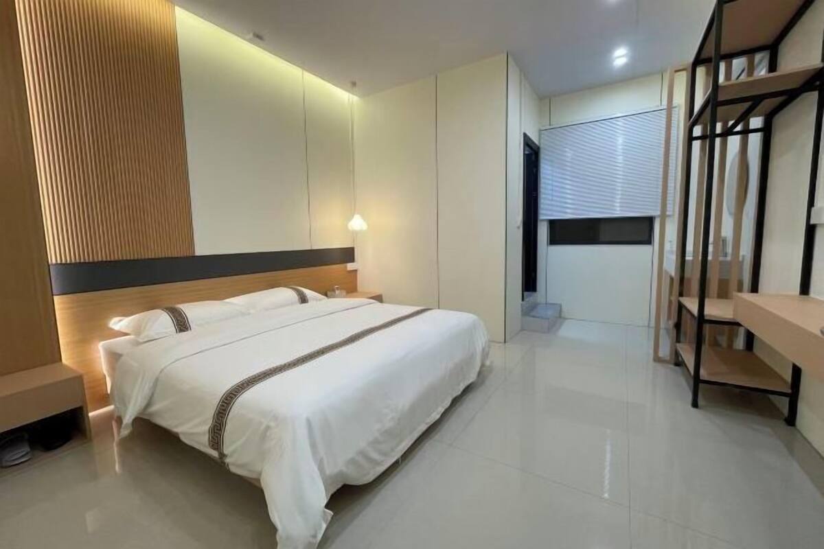 A modern hotel room with a large bed, a desk, and a wardrobe.