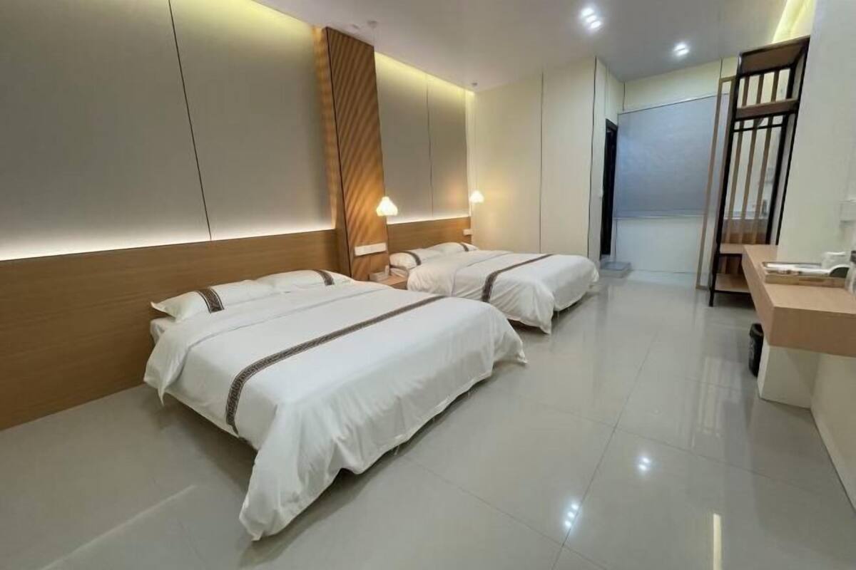 A hotel room with two beds, a wooden headboard, a desk, and a mirror.
