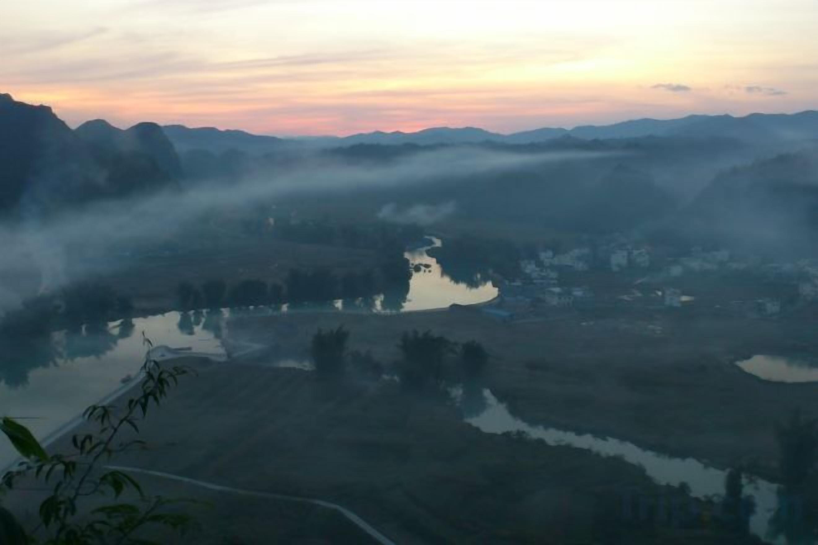 A misty landscape with a river and surrounding hills.