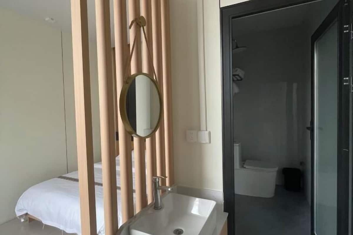 A bathroom with a white sink, a mirror, and a toilet visible through a glass door.