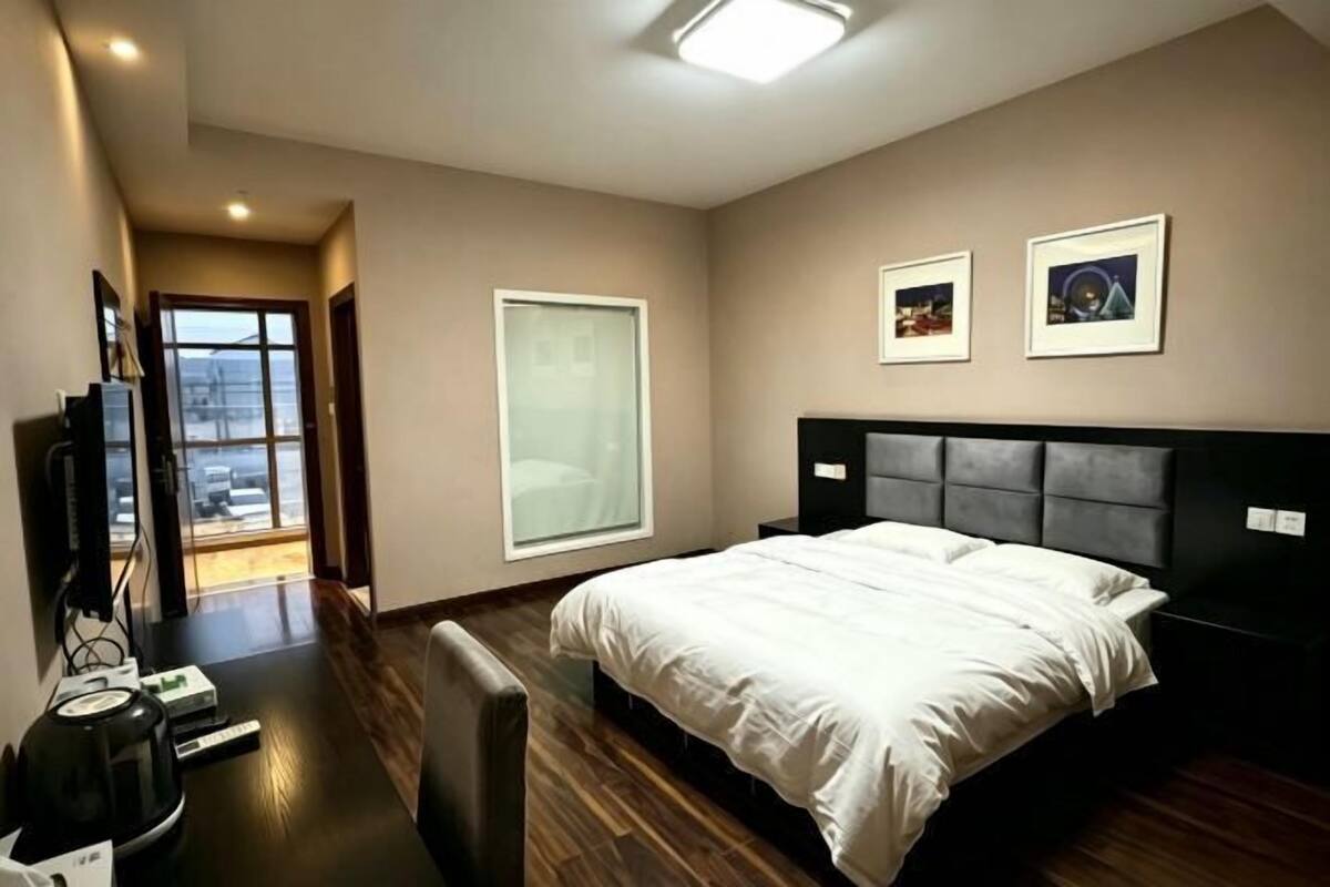 A bedroom with a bed, a desk, a chair, a TV, and a window.