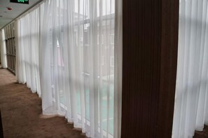 Un pasillo con cortinas blancas y translúcidas, piso de madera y un área exterior visible a través de las ventanas.