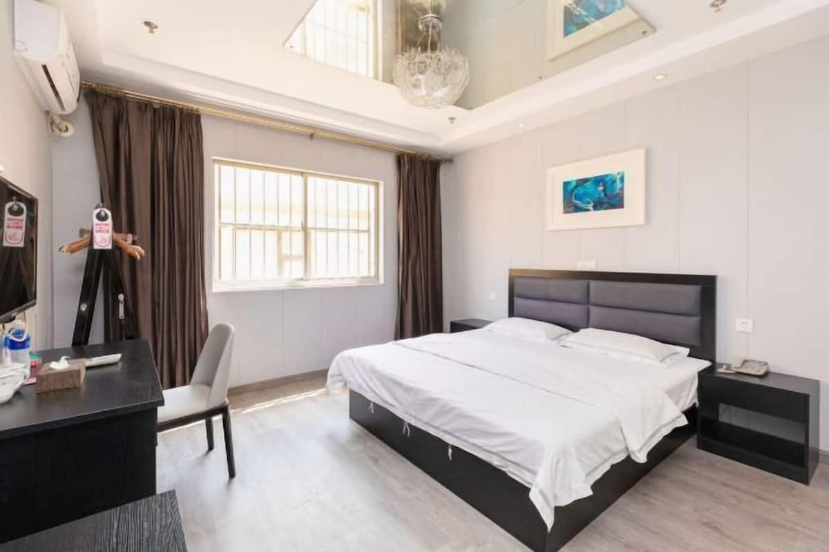 A modern hotel room with a large bed, a desk, a chair, a TV, and a window with curtains.