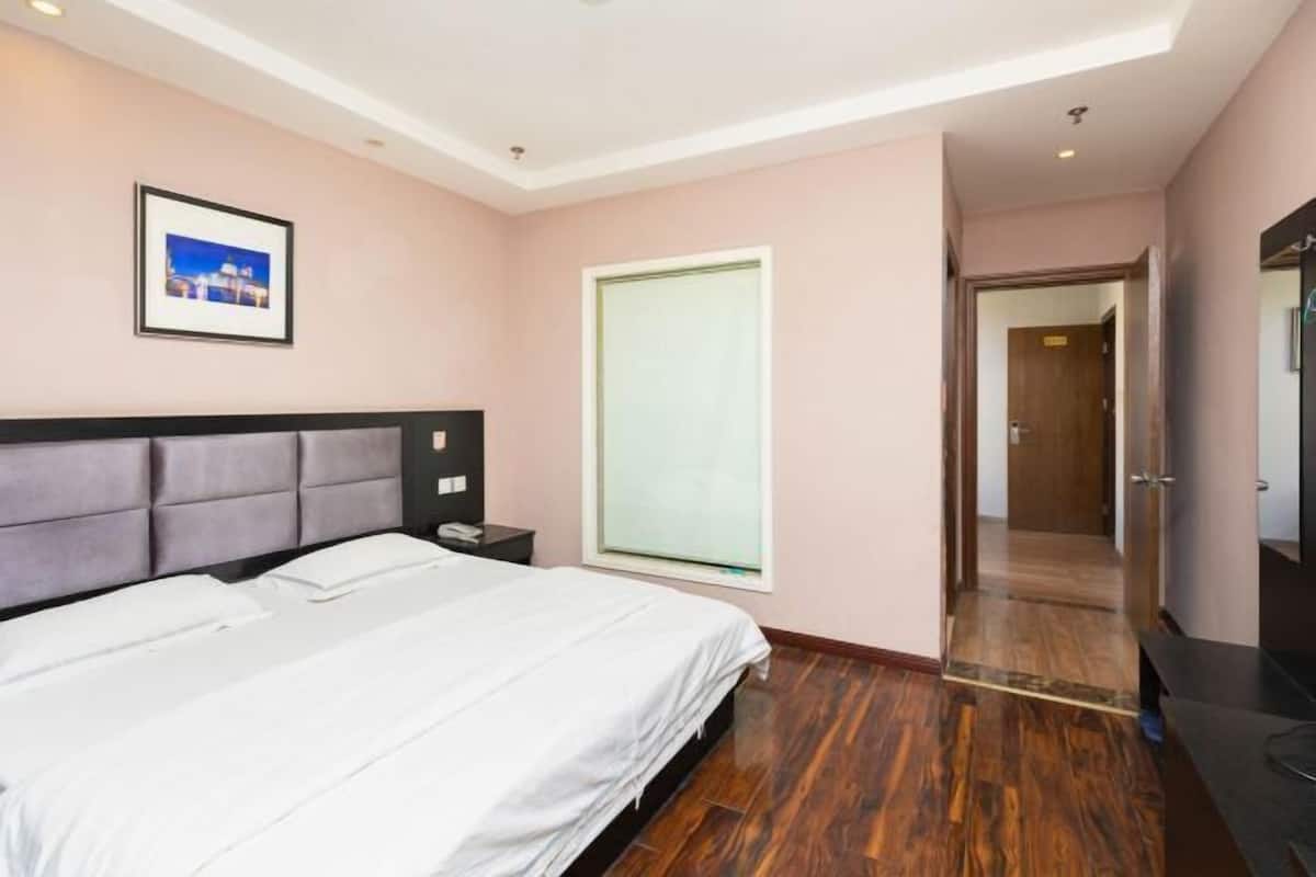 A bedroom with a bed, a nightstand, a framed picture on the wall, and a door leading to another room.