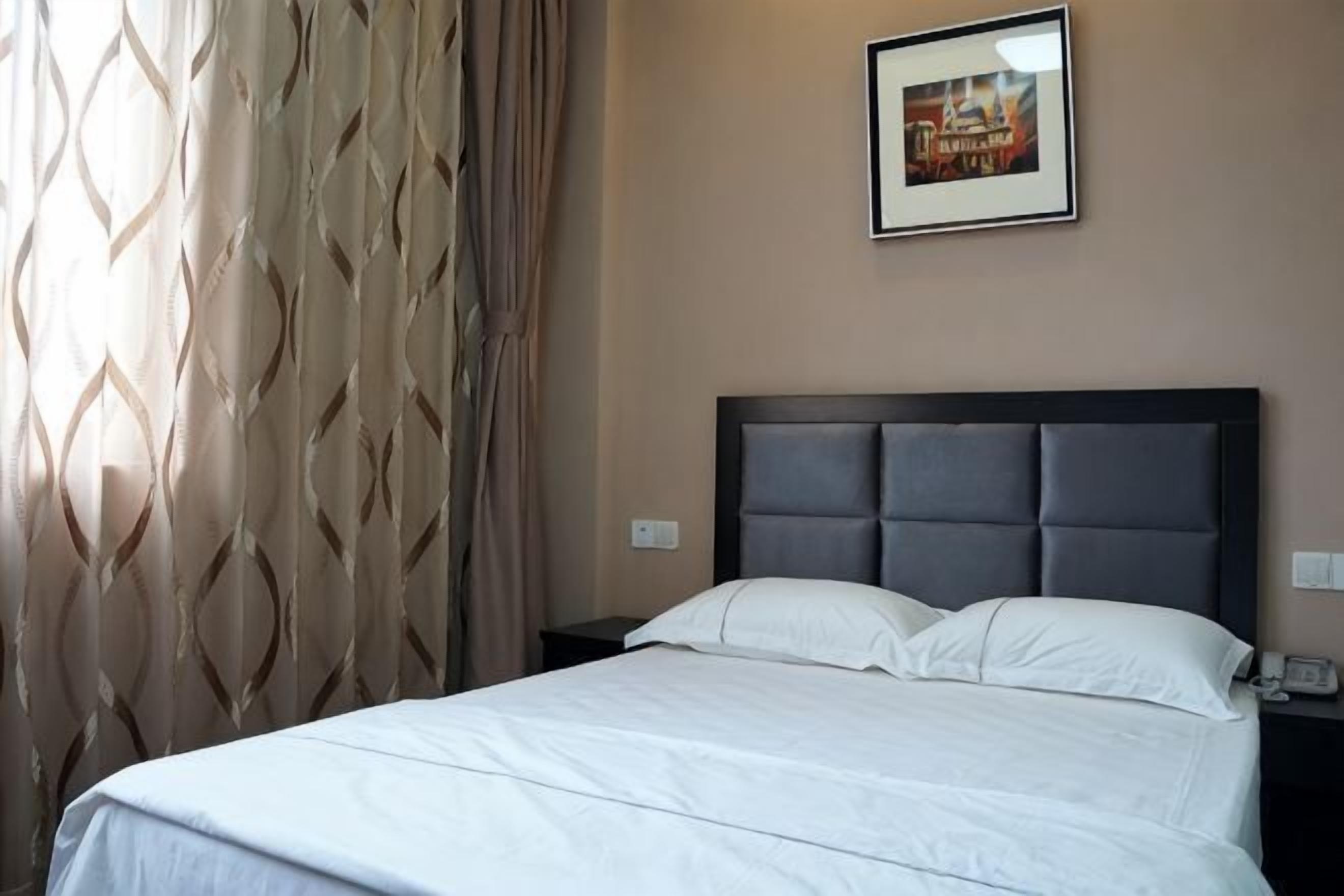 A neatly made bed with a headboard, a nightstand with a phone, and a wall-mounted picture.