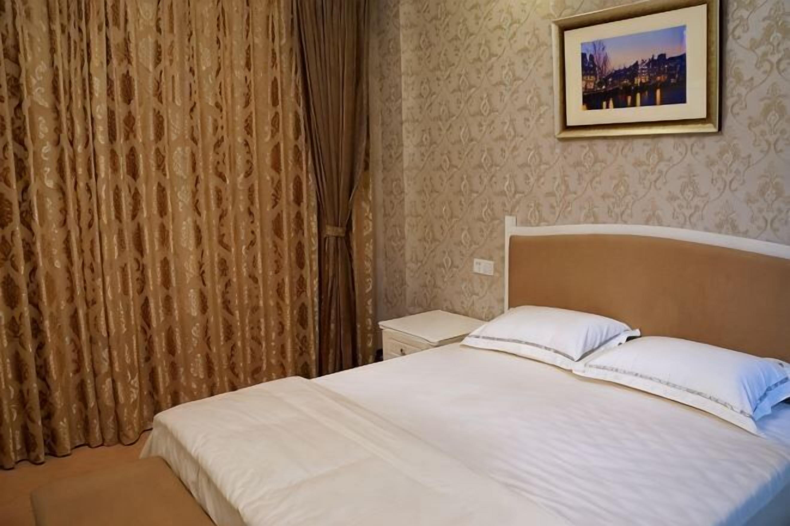 Ein Hotelzimmer mit Bett, Vorhängen, einem Nachttisch und einem gerahmten Bild an der Wand.