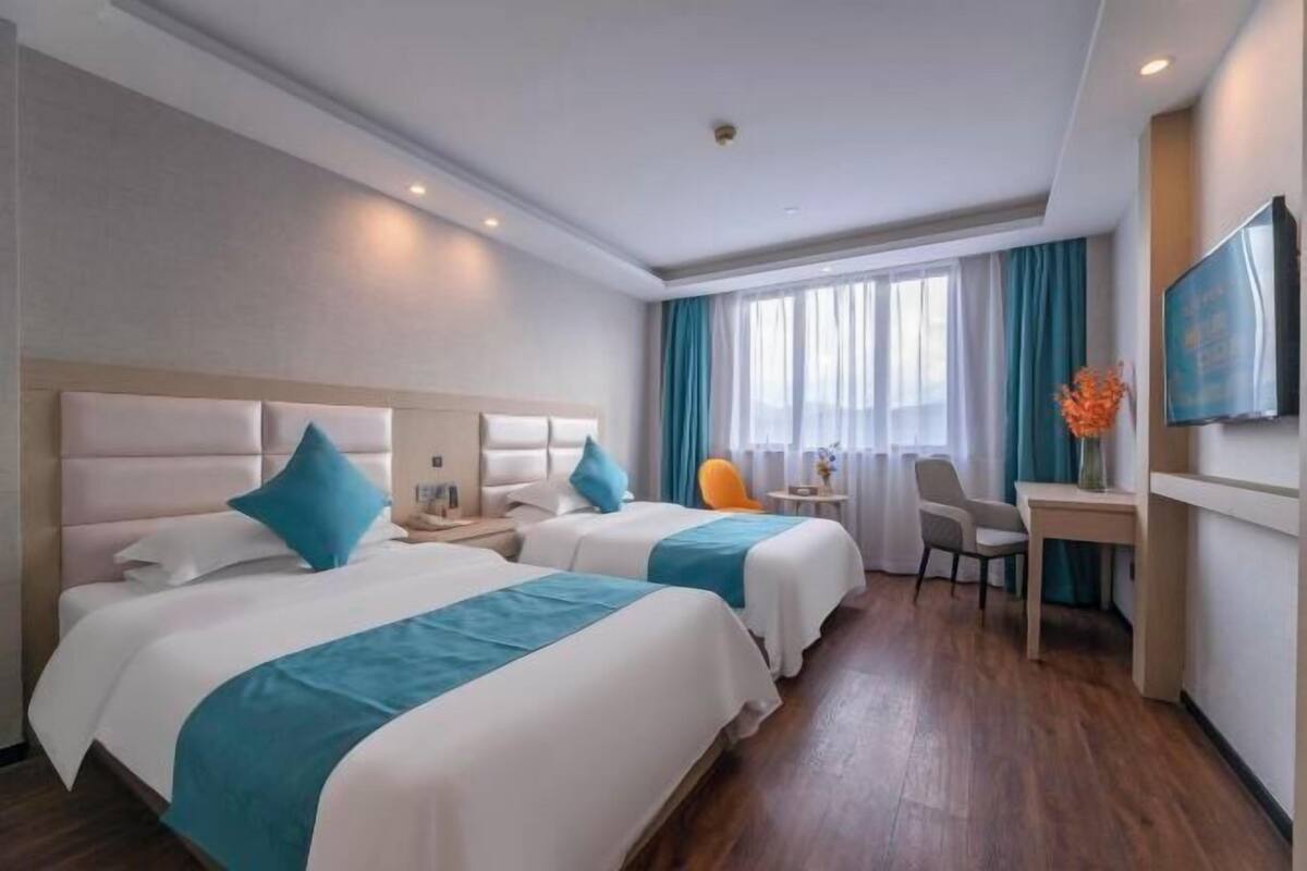 A hotel room with two beds, a desk, a chair, a TV, and a window with curtains.