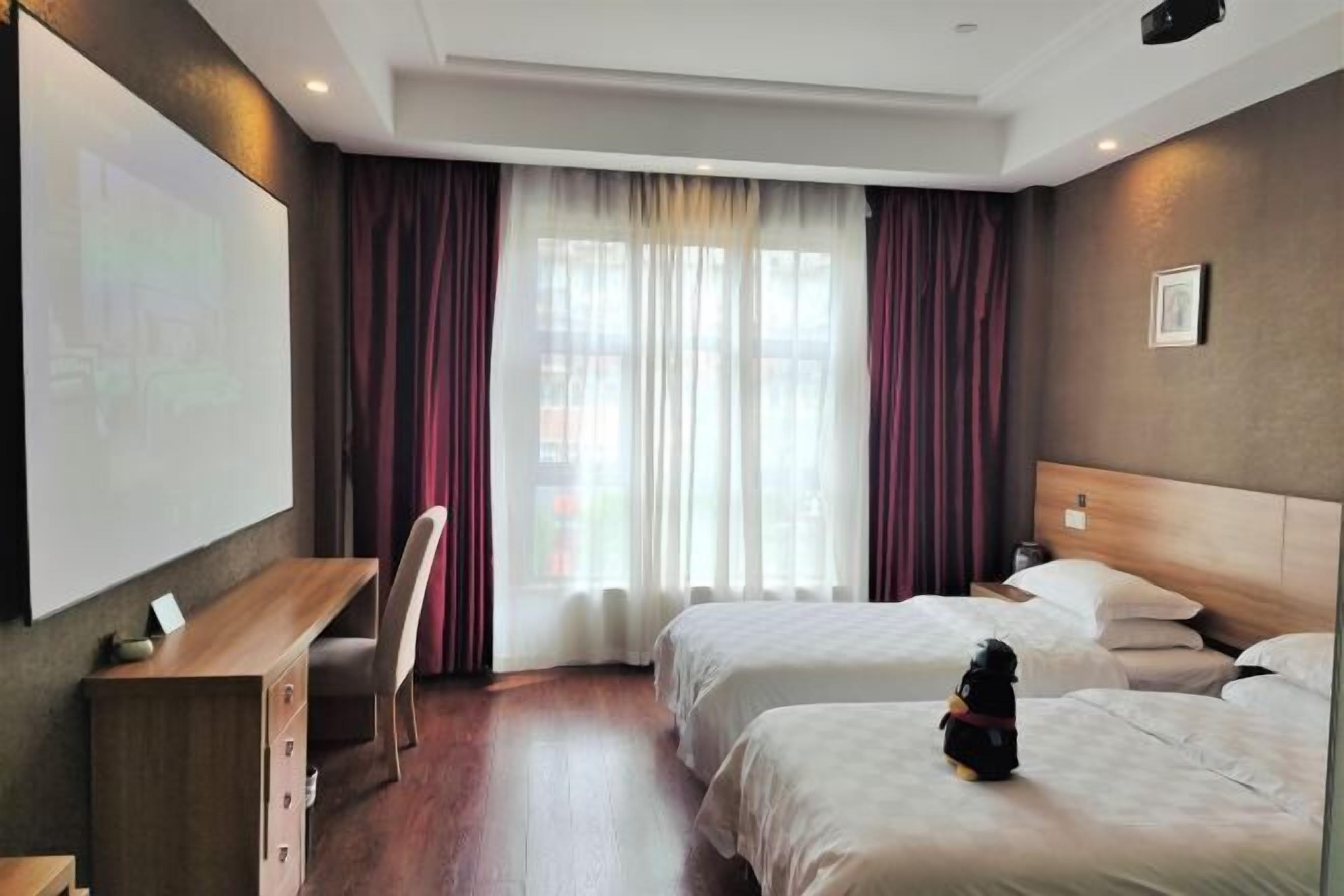 A hotel room with two beds, a desk, a chair, and a large window with curtains.