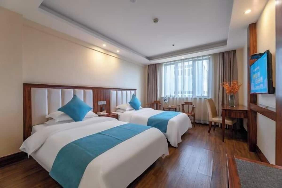 A hotel room with two beds, a desk, a chair, a TV, and a window with curtains.
