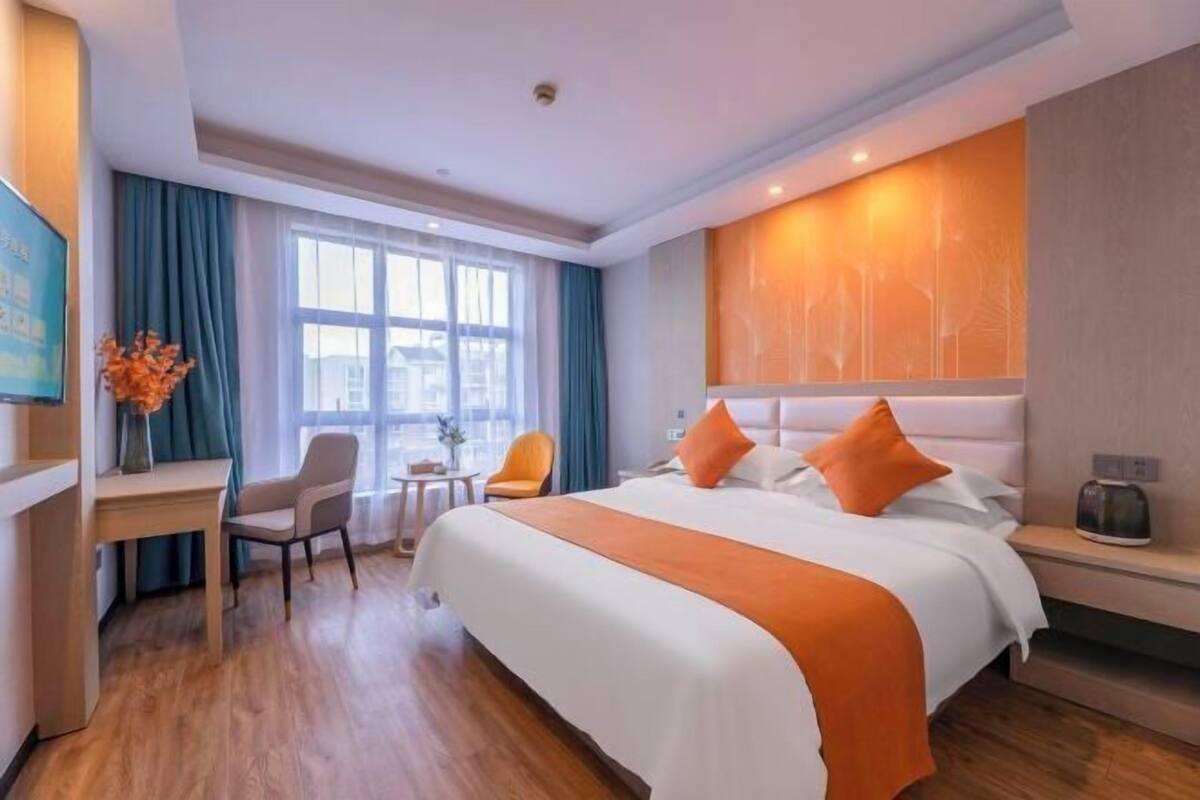 A hotel room with a large bed, a desk, two chairs, a small table, and a window with curtains.