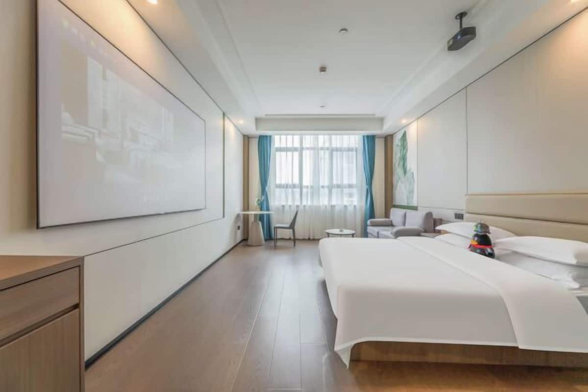 A hotel room with a bed, a desk, a chair, a small table, and a window with curtains.
