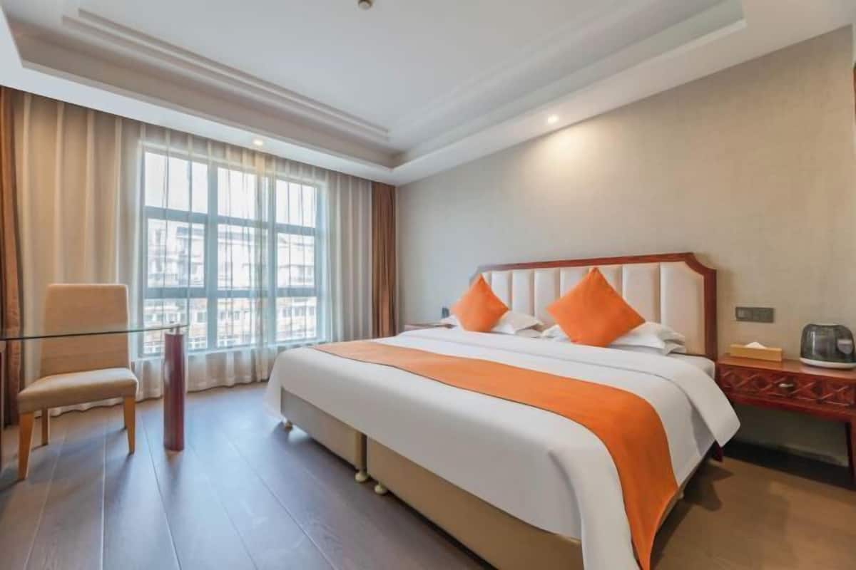 A hotel room with a large bed, a chair, a desk, and a window with curtains.