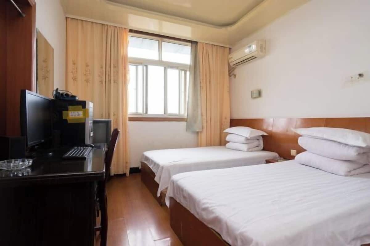 Hotellihuone, jossa on kaksi erillistä sänkyä, työpöytä tietokoneella, televisio ja ikkuna, jossa on verhot.