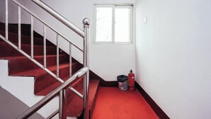 A staircase with red carpeted steps and a metal handrail, leading to a room with a window and a fire extinguisher on the floor. - Fanchang Yichun Hotel (Wuhu)