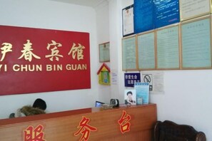 A reception desk with a red sign, a bulletin board with notices, and a small house decoration.