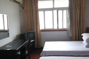 Una habitación de hotel con cama, escritorio con televisor y ventana con cortinas.