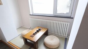 Une petite pièce au sol recouvert de tatamis, une basse table en bois avec un service à thé, deux tatamis et un radiateur.