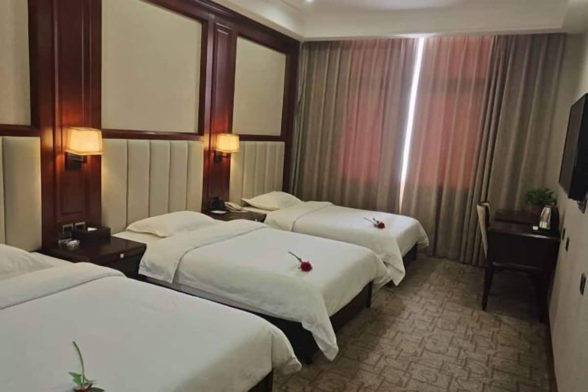 Une chambre d’hôtel avec trois lits, un bureau, une chaise et un téléviseur.