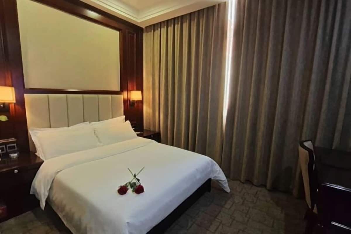 Une chambre d’hôtel avec un lit, une table de chevet, une lampe et une grande fenêtre avec des rideaux.