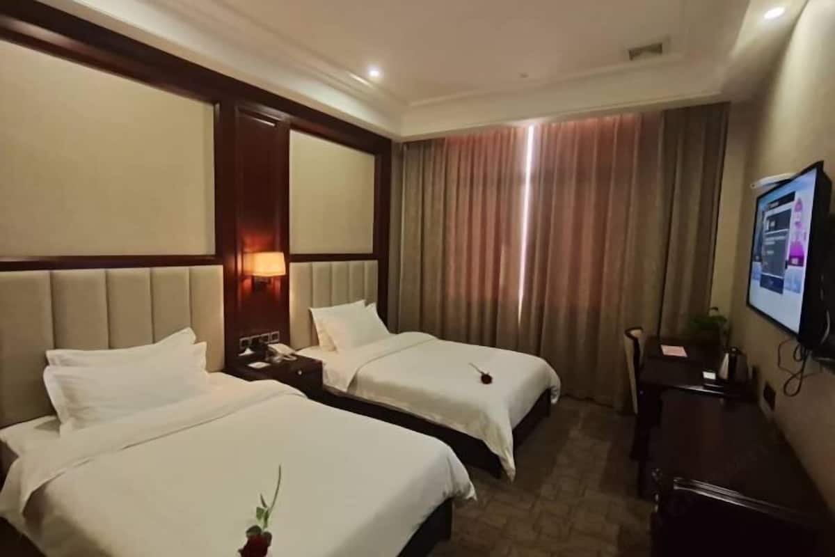 Une chambre d’hôtel avec deux lits, une télévision, un bureau et une fenêtre avec des rideaux.