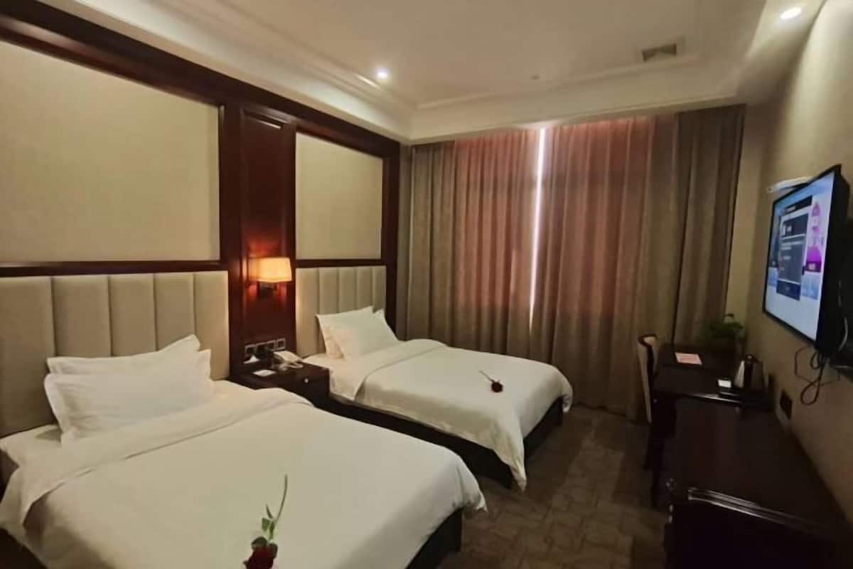 Une chambre d’hôtel avec deux lits, une télévision, un bureau et une fenêtre avec des rideaux.