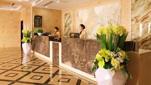A hotel reception area with marble reception desks, a geometric patterned floor, and floral centerpieces. - YinXiang changchun (Huixian)