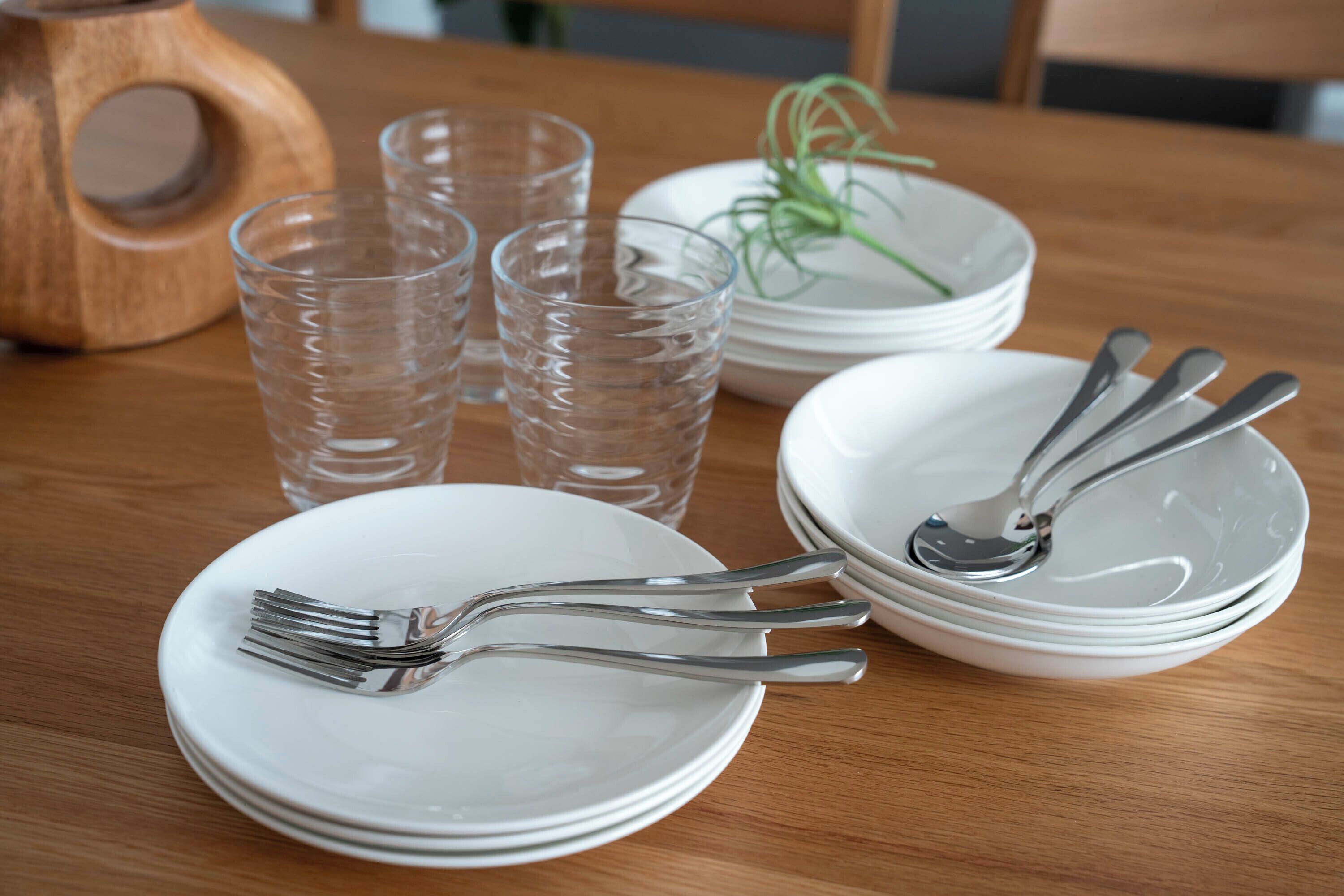 A dining table with stacked white plates, forks, and a spoon.