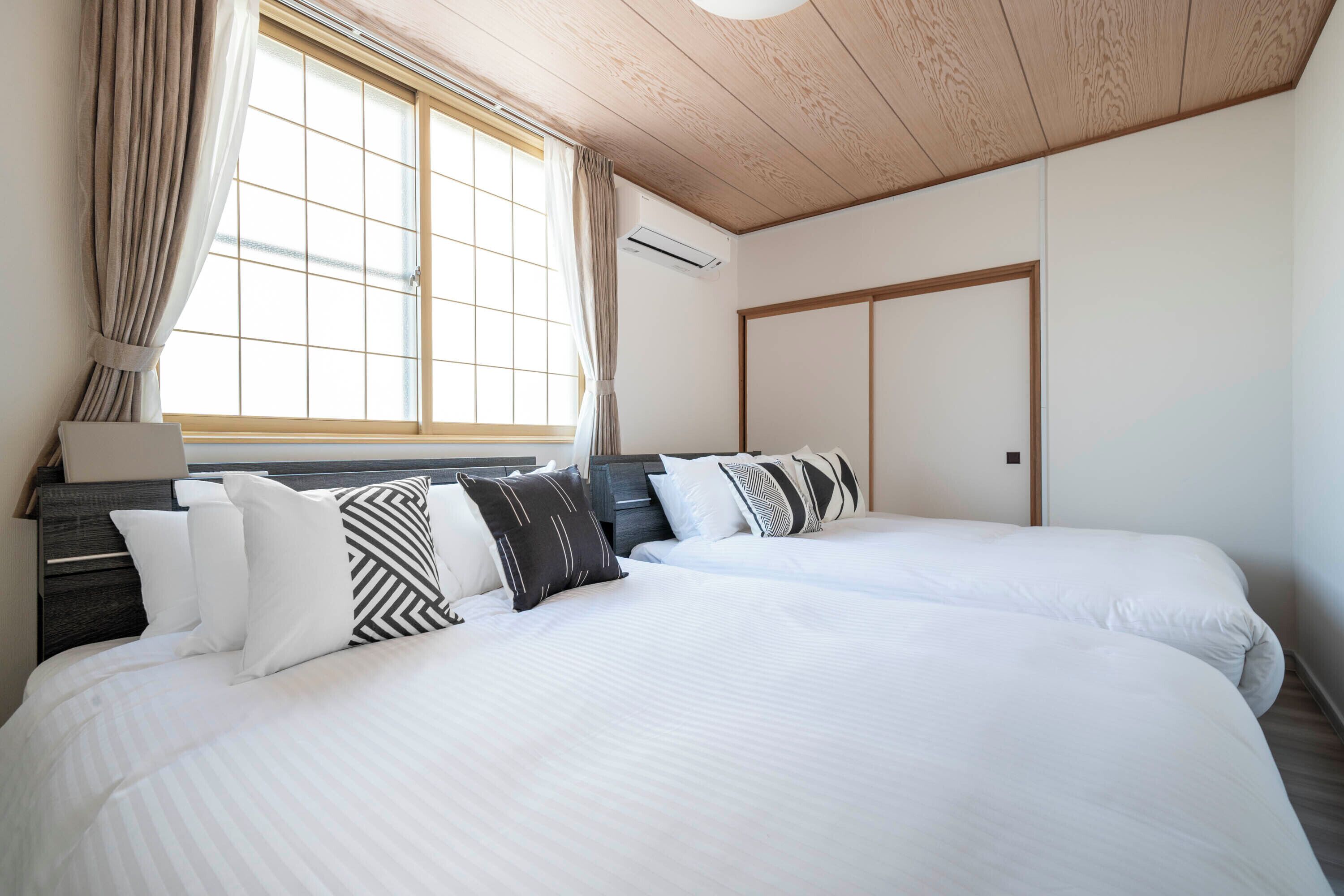 Ein Hotelzimmer mit zwei Betten, einem Vorhangfenster, einer Holzbalkendecke und einem Kleiderschrank.