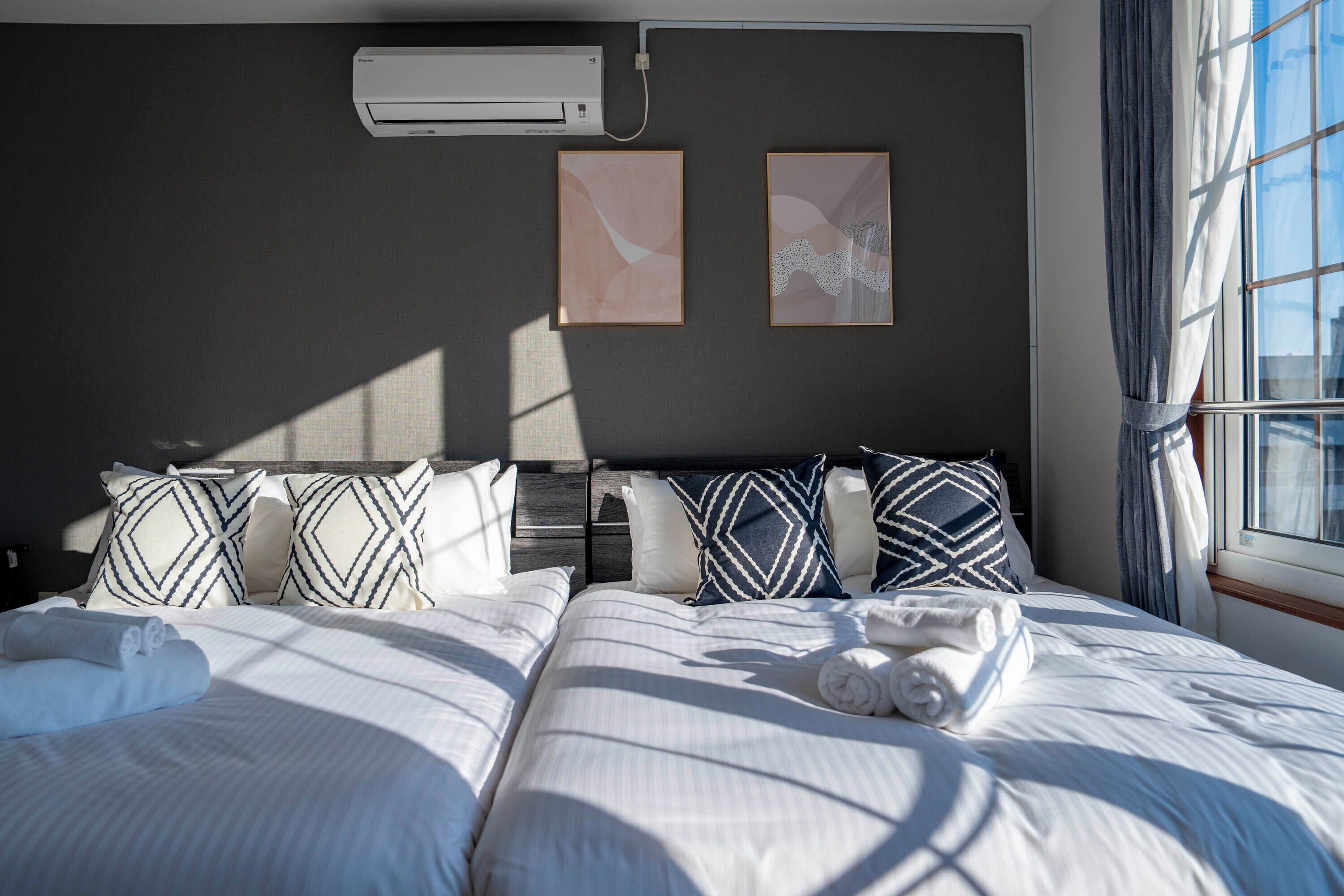 A hotel room with two beds, a large window with curtains, and artwork on the wall.