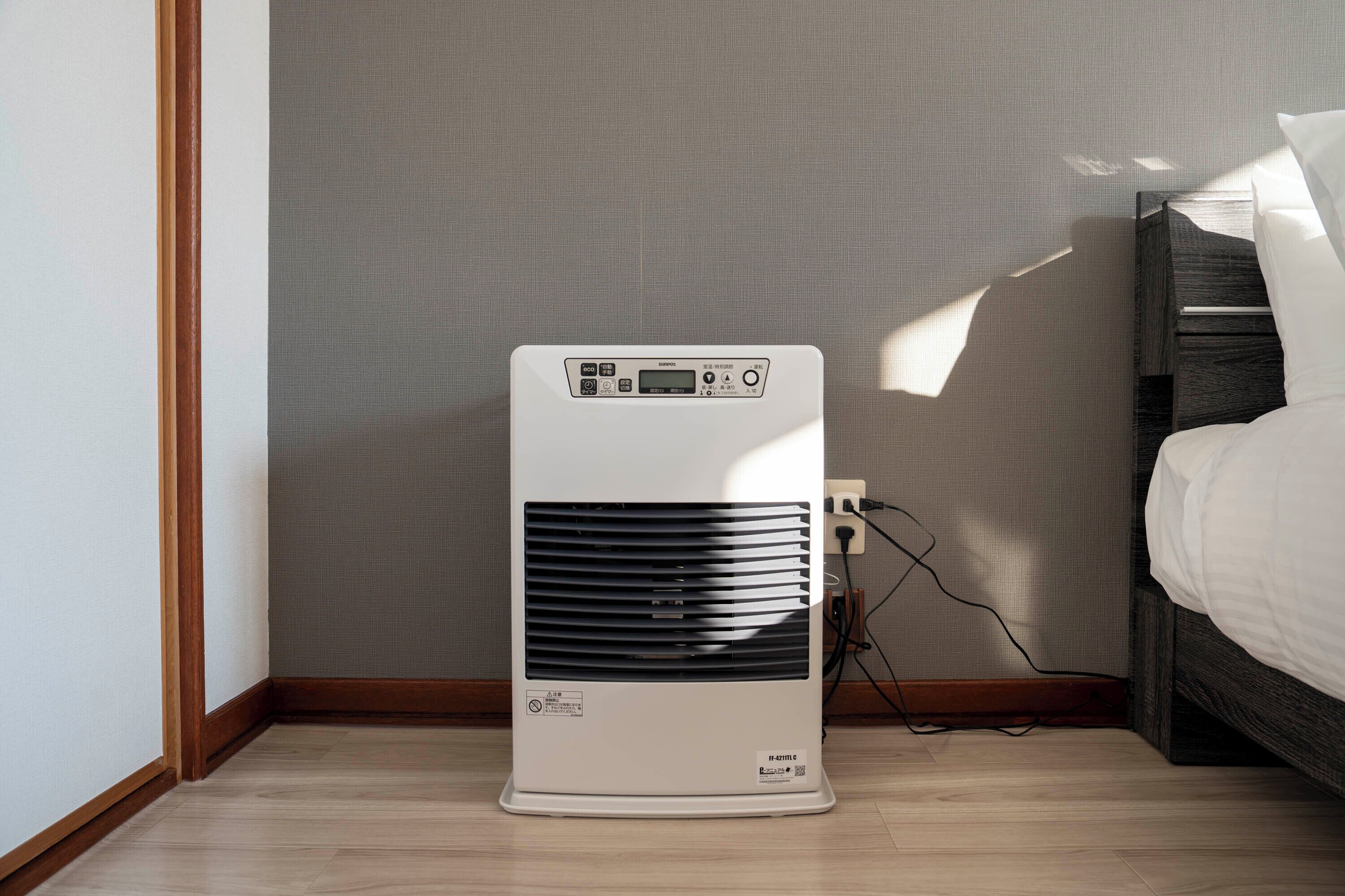 Een draagbare airconditioner in een kamer met een houten vloer, een bed en een stopcontact.