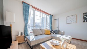 Ein modernes Wohnzimmer mit einer Couch, einem Couchtisch, einem Fernseher und einem Fenster mit Vorhängen.