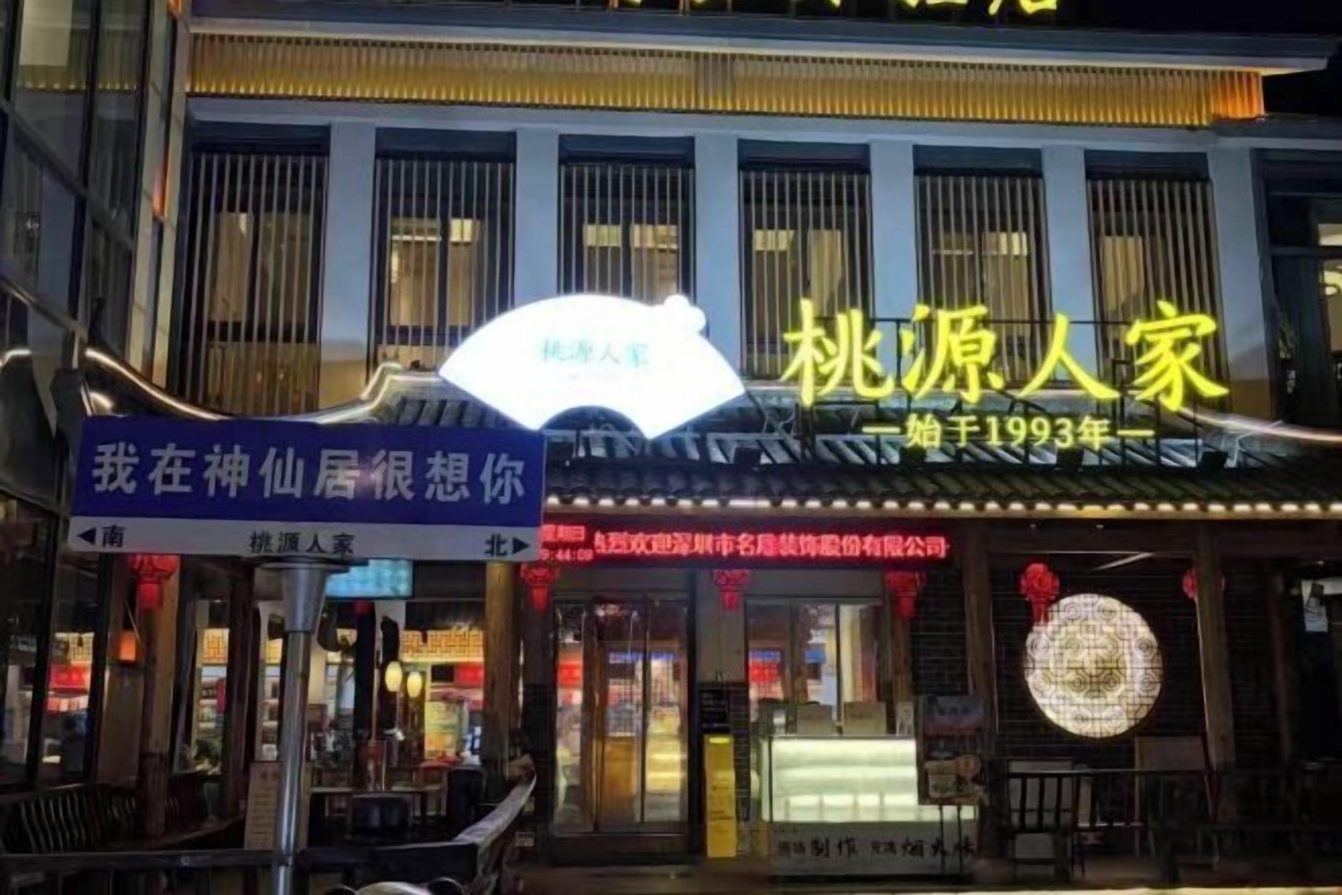 Um edifício com uma placa que diz '桃源人家' e outra placa com a mensagem 'Sinto sua falta, morando entre deuses'.
