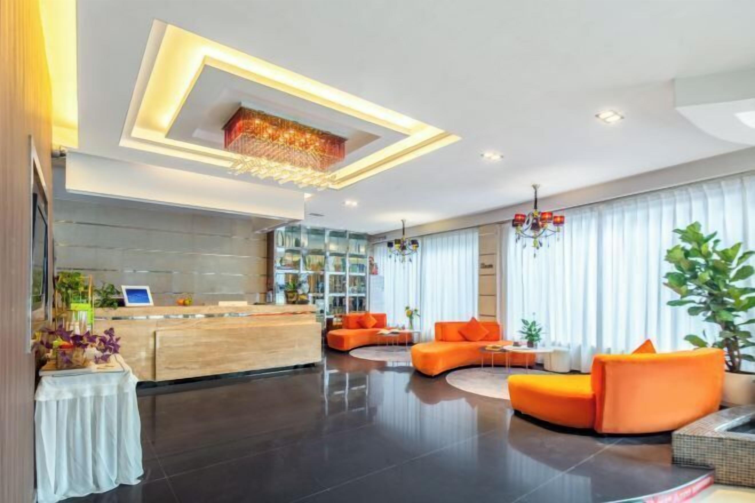 Un hall d’hôtel moderne avec un comptoir d’accueil, un espace détente aux couleurs orangées et un lustre.