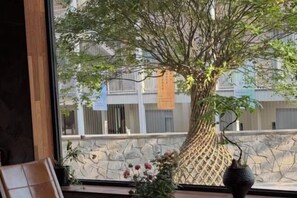 A large tree with a lattice trunk structure, placed in front of a window with a stone wall and buildings in the background. - Xianju Nanxingyuan Boutique Hotel (Wuyue Plaza) (Xianju)