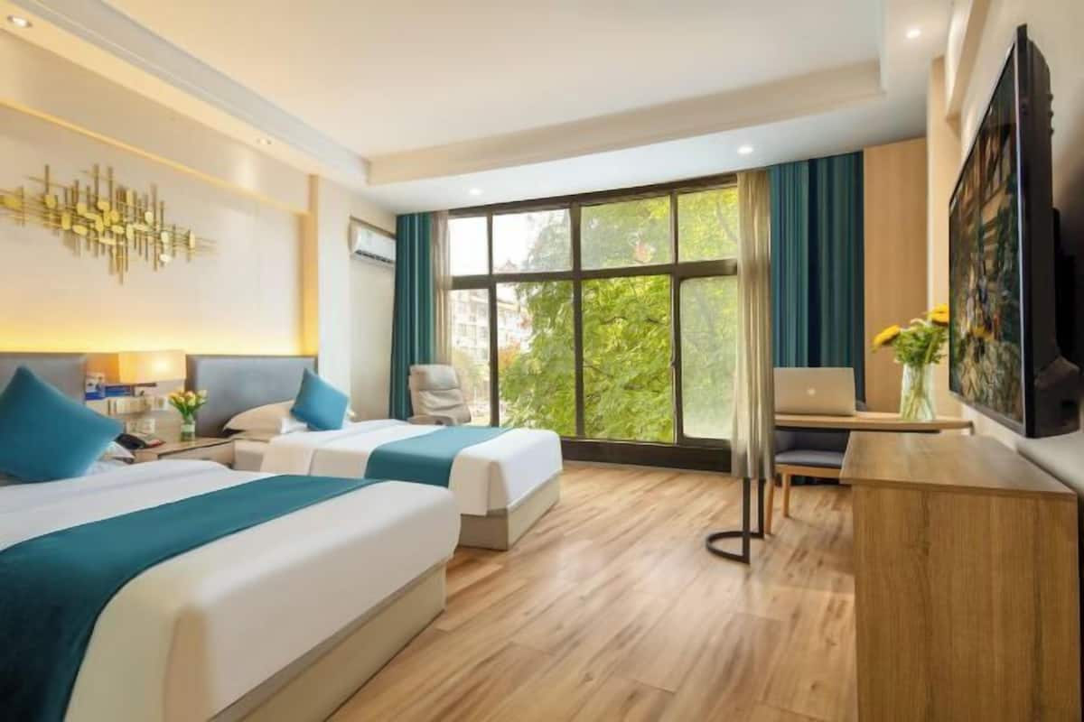 A hotel room with two beds, a desk, a TV, and a large window.