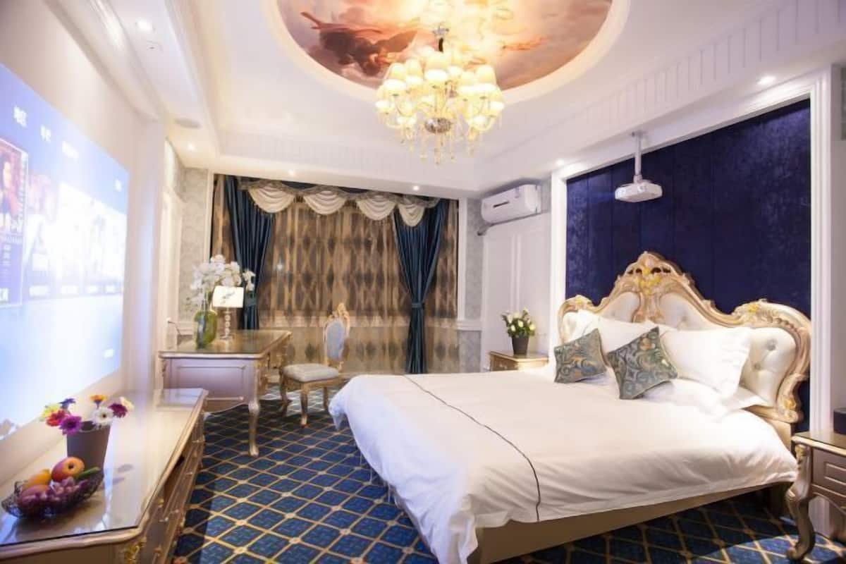 A hotel room with a large bed, a chandelier, a desk with a chair, and a television screen.