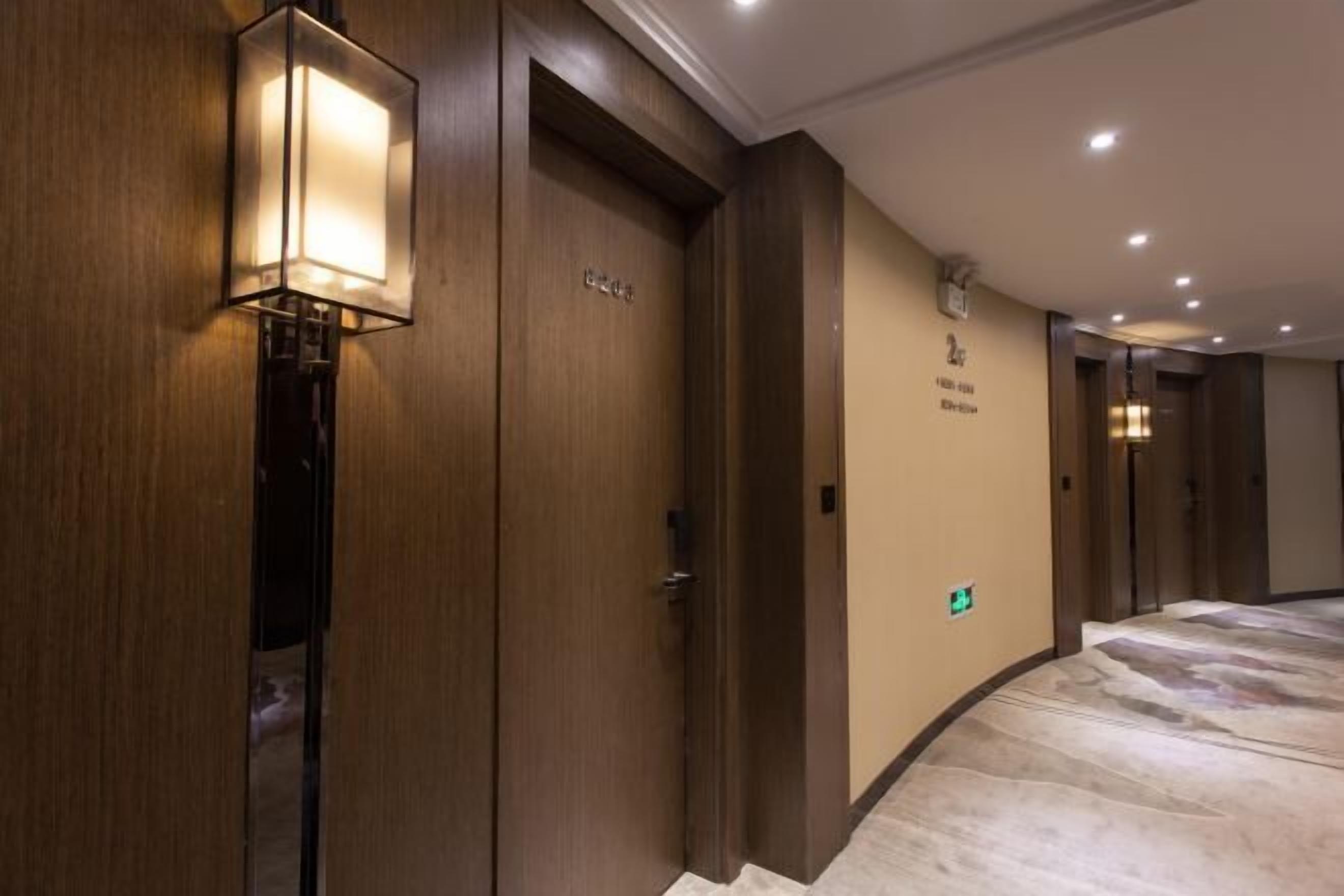 Un pasillo de hotel con puertas de madera, una lámpara fijada a la pared y suelo de mármol.