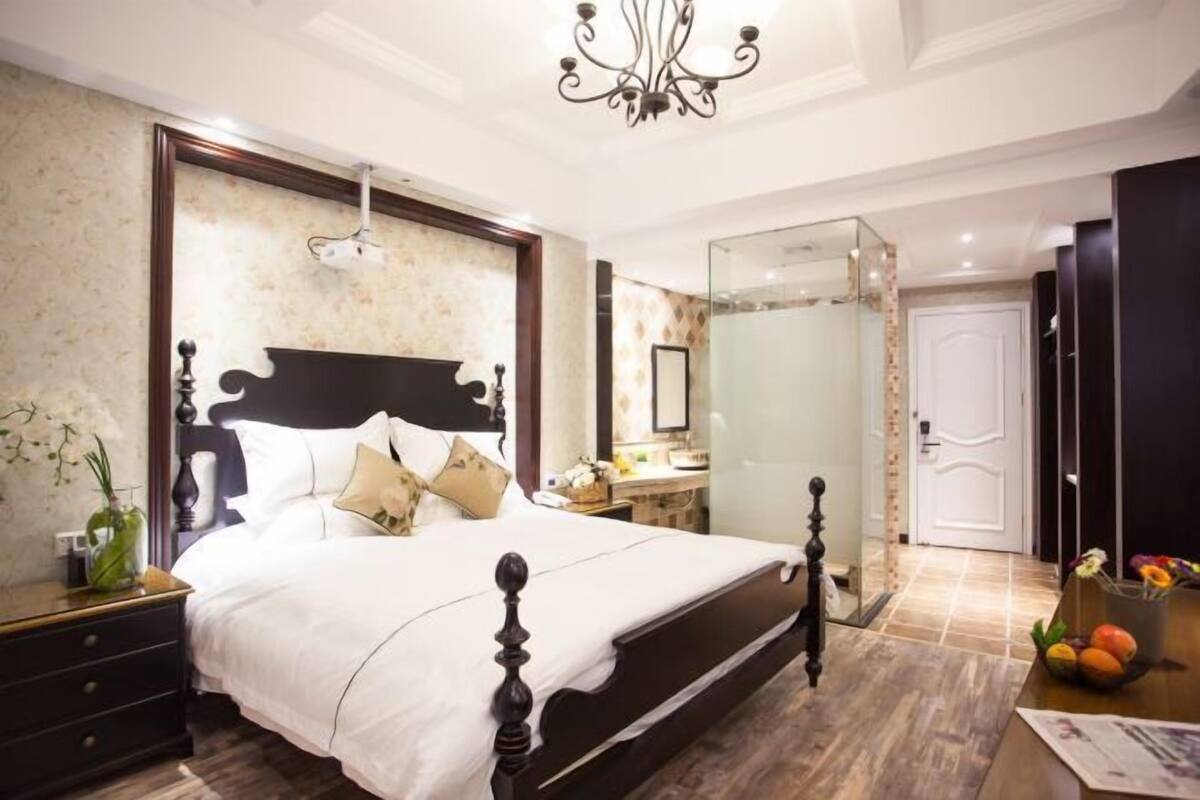 A bedroom with a large bed, a nightstand, a dresser, a mirror, and a chandelier.