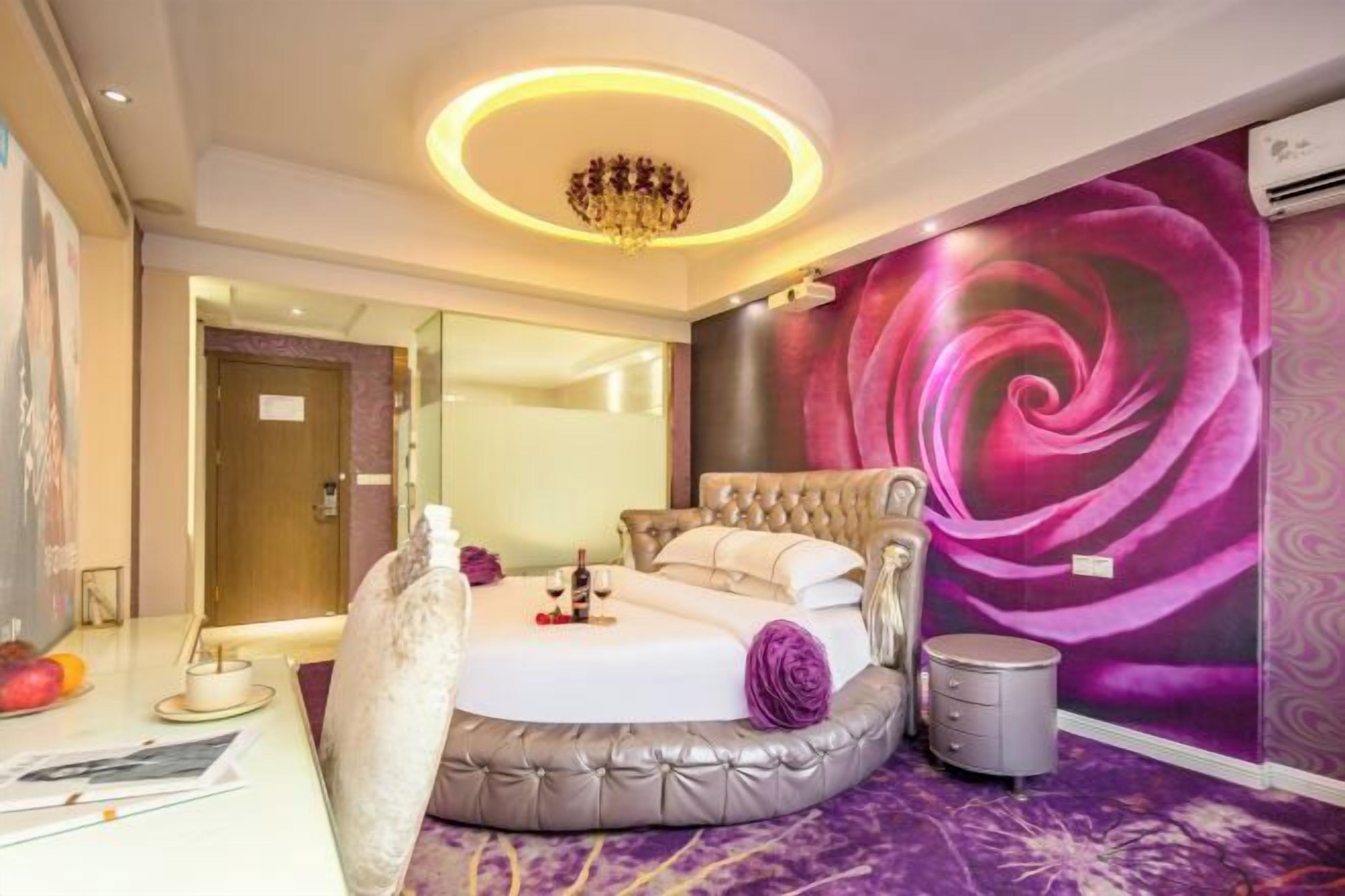 A bedroom with a round bed, a chandelier, a large floral mural, and a small bedside table.