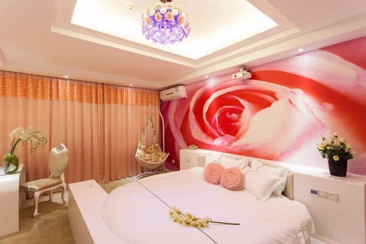 A bedroom with a large bed, a chandelier, a wall mural, a desk, and a chair.