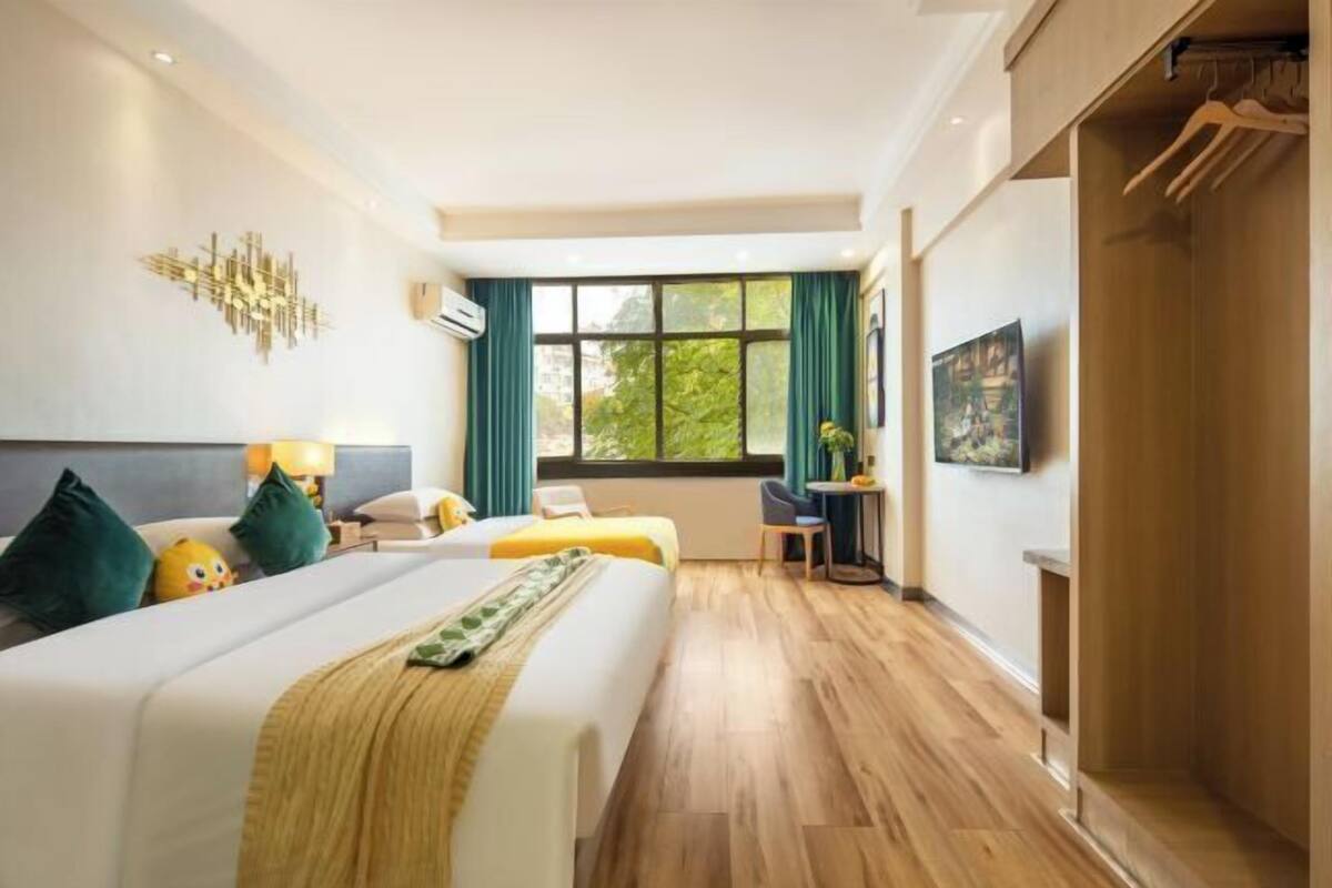 A hotel room with a large bed, a desk, a chair, a window with curtains, and a painting on the wall.