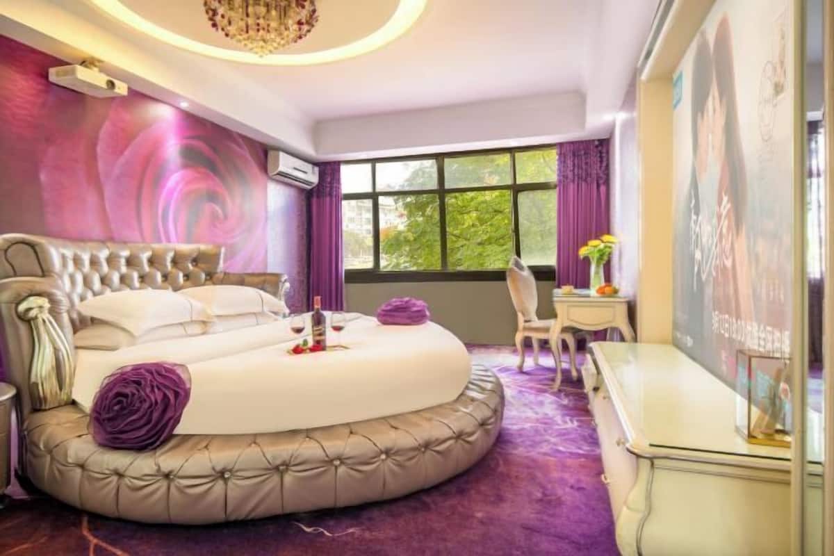 A circular bed with a tufted headboard, a small table with a vase of flowers, and a desk with a chair.