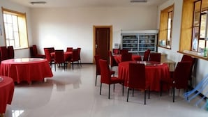 Un comedor con mesas redondas y sillas rojas, piso de baldosas blancas y una ventana con vistas.