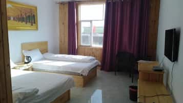 A room with two beds, a desk, a chair, a television, and a window with curtains.