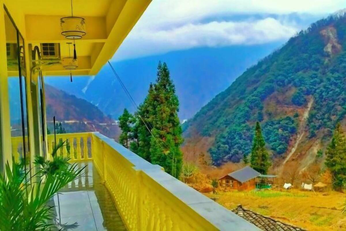 Ein Balkon mit Blick auf eine gebirgige Landschaft, eine kleine Holzhütte und ein klarer Himmel.