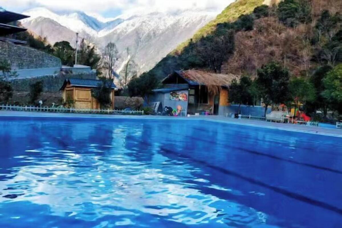 Ein Schwimmbecken mit Bergblick, traditionellen Gebäuden und einer Umzäunung.